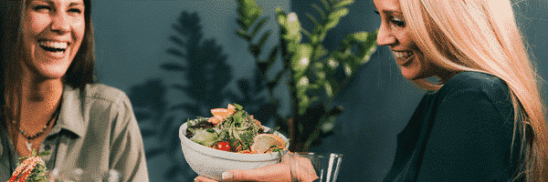 Two women smile while eating vegetarian food